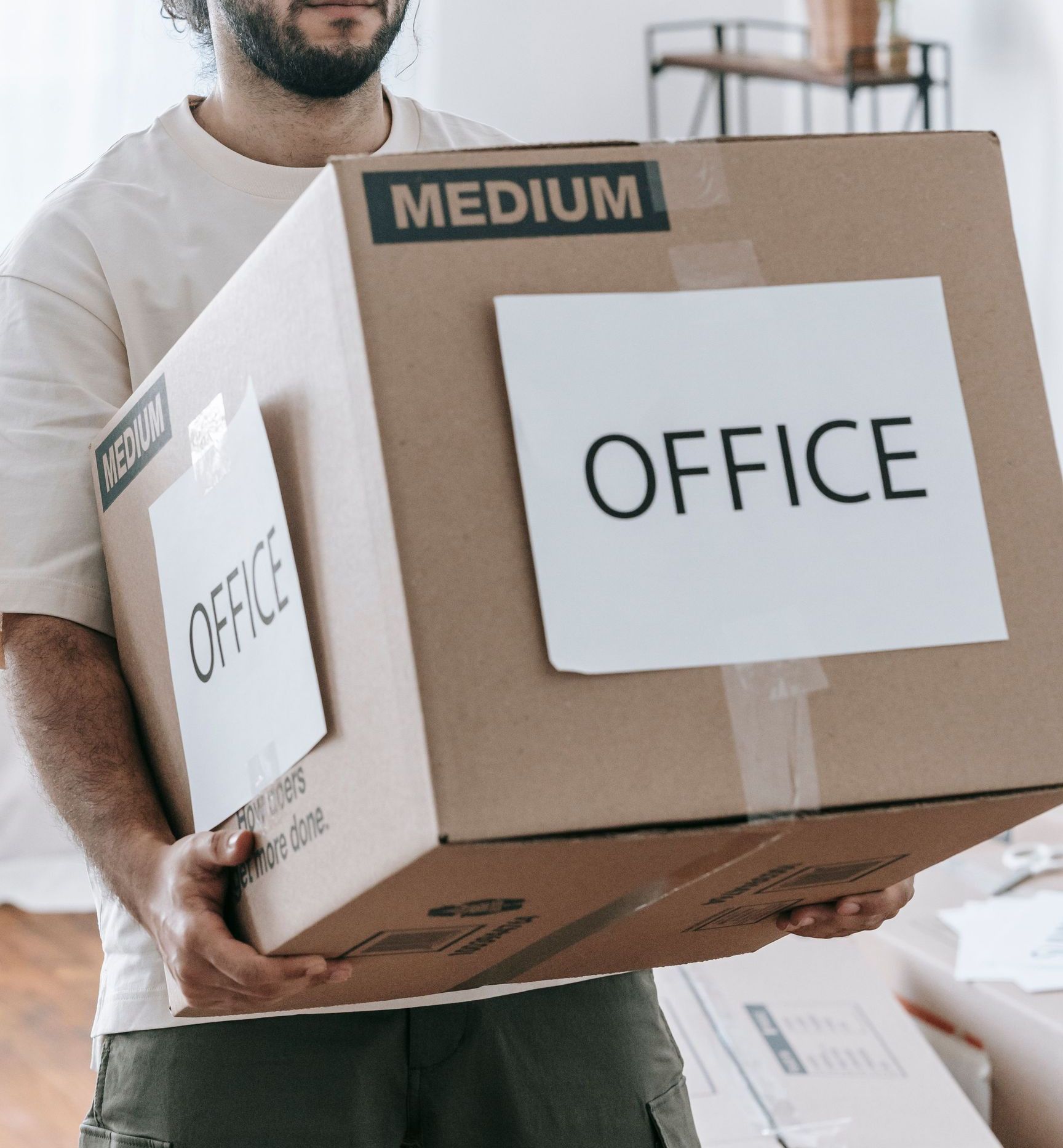 Man moving box labeled 'Office' indoors during relocation or packing.