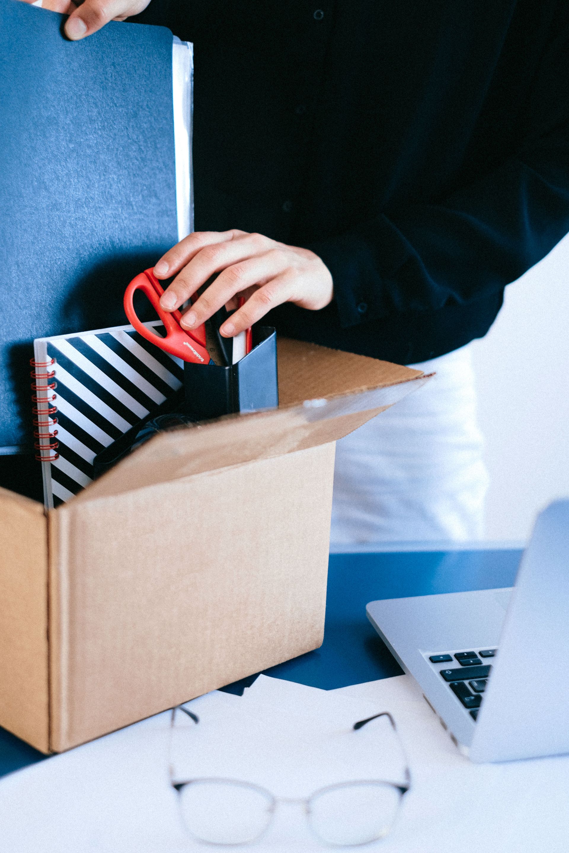 Person organizing office essentials into a box, focusing on decluttering workspace.